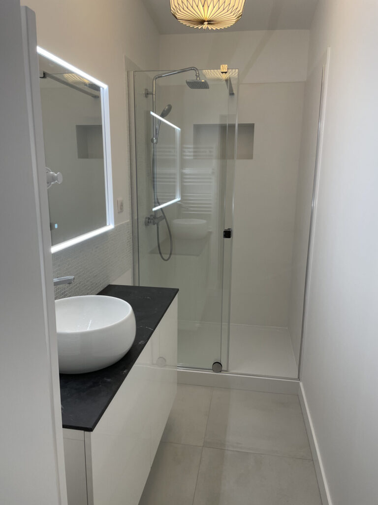 salle de bain rénovée dans les tons blanc avec cabine de douche, miroir rétroéclairé et vasque arrondie