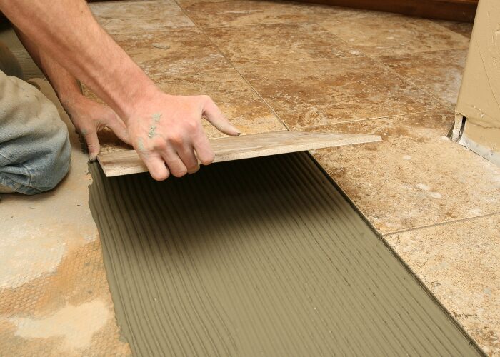 zoom sur les main d'un artisan en train de poser une plaque de carrelage
